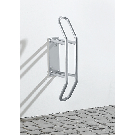 Soporte de bicicleta metálico en una pared blanca, adoquines debajo.