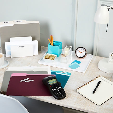 Bureau avec dossiers, porte-stylos, horloge et étiqueteuse. L'étiquette indique 'Nouveaux clients'.