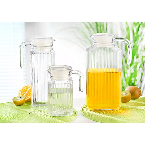 Drie glazen kannen met water en sap, plus kiwi en sinaasappel op groene matten.
