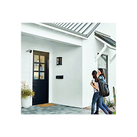 Zwei Frauen gehen auf ein Haus zu, an der Hauswand ist eine Überwachungskamera angebracht.