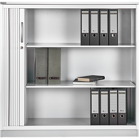 Archivo blanco con puerta de lamas, varios estantes y carpetas. Hay un libro en un estante.