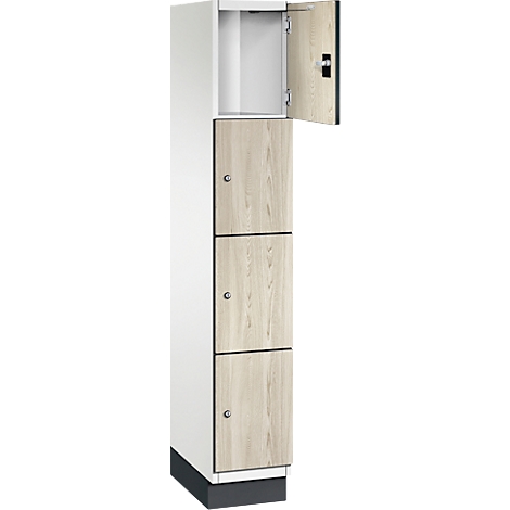 Armoire à trois compartiments, aspect bois clair, une porte ouverte. Au-dessus des compartiments, un compartiment blanc ouvert.