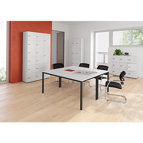 Salle de conférence avec table blanche, chaises noires et armoires blanches.