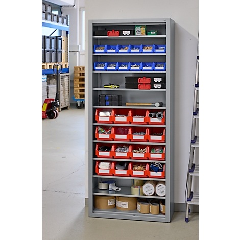 Étagère en métal avec des bacs rouges et bleus, remplis d'outils. Un atelier est visible en arrière-plan.