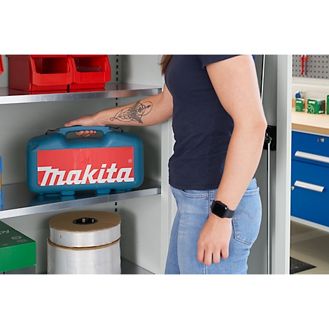 Une personne en jean et t-shirt bleu foncé se tient près d'une armoire. Sur l'étagère se trouve une boîte à outils bleue Makita.