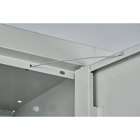 Gros plan : câble métallique sur une porte d'armoire, gris clair. L'armoire est ouverte.
