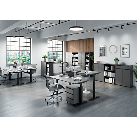 Un bureau avec des bureaux et des chaises gris, des classeurs, des meubles de bureau, des plantes, des fenêtres, des horloges et de l'art sur le mur.
