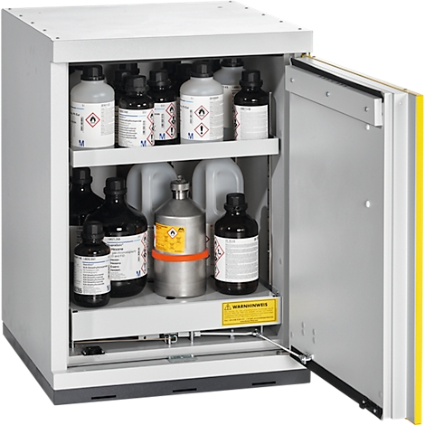 Armoire ouverte avec des bouteilles de produits chimiques, dont des étiquettes de substances dangereuses. Panneaux d'avertissement jaunes. La porte est partiellement ouverte.