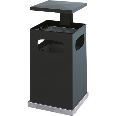 Black, rectangular waste container with a lid and cutouts. It stands on a concrete base.