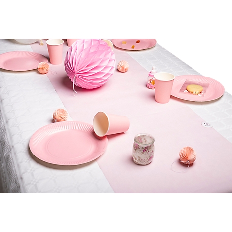 Une table dressée de manière festive avec des assiettes, des tasses et des décorations roses. Un chemin de table rose et une grande boule en papier sont sur la table.