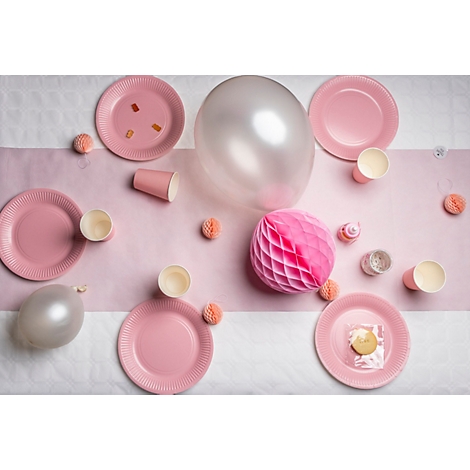 Vue de dessus d'une surface de table décorée pour une fête : assiettes et tasses roses, ballons et éléments décoratifs.