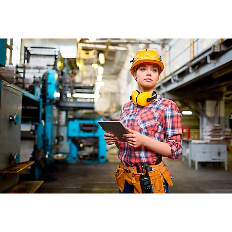 Jeune femme dans un atelier avec une tablette et un casque de sécurité. Regardant au loin, prête à travailler.