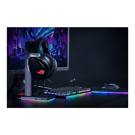 Schwarzes Gaming-Headset mit Mikrofon auf Halterung, leuchtende Tastatur, Maus, Bildschirm.