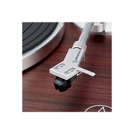 Nahaufnahme eines silbernen Audio-Technica Tonabnehmers über einer hölzernen Plattenspieleroberfläche.