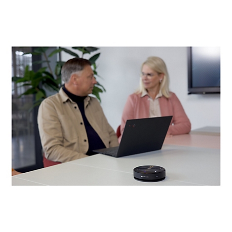 Zwei Personen sitzen an einem Tisch. Auf dem Tisch liegt ein Laptop und ein schwarzer Lautsprecher.
