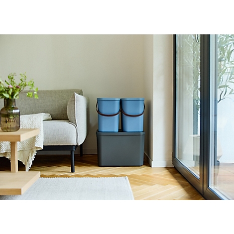 Hellblau Eimer mit braunen Griffen stehen auf einem grauen Abfalleimer. Wohnzimmer mit Fenster und Sofa.