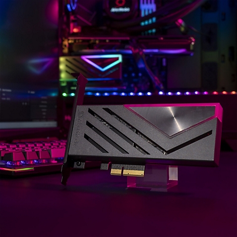 Schwarze AVerMedia PCIe-Capture-Karte vor einem Gaming-PC mit pinker Beleuchtung.
