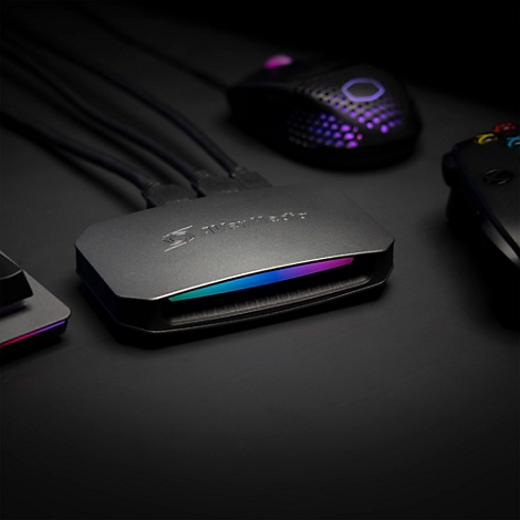 AVerMedia Capture Card mit RGB-Lichtstreifen auf einem Schreibtisch neben Gaming-Maus und Controller.