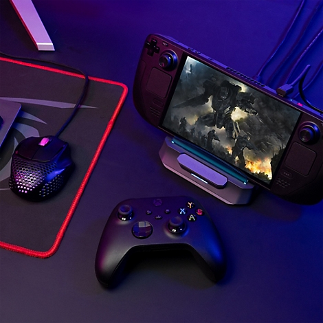 Handheld-Konsole in Dockingstation auf Schreibtisch mit Controller und Maus, beleuchtet durch blaues Licht.