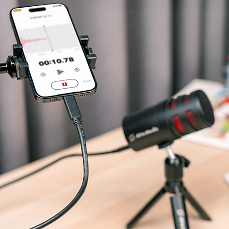 Smartphone in Halterung mit Audio-Aufnahme-App verbunden mit einem schwarzen Mikrofon auf einem Stativ.
