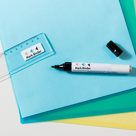 Een witte permanente marker met zwarte punt en dop ligt naast een liniaal en gekleurd papier.