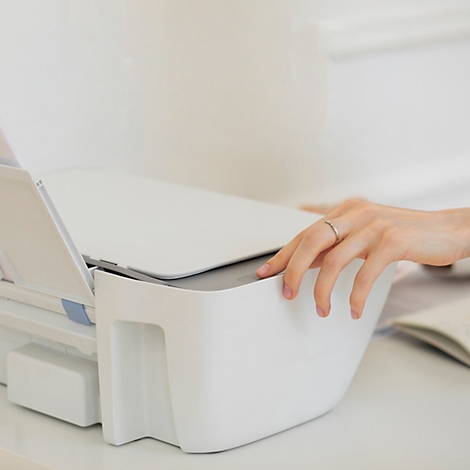 Main actionnant une imprimante blanche moderne sur un bureau lumineux.