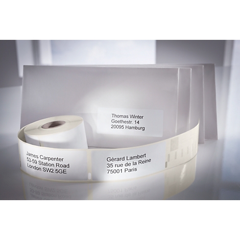 A roll of white labels with addresses printed on them. Envelopes are visible in the background.