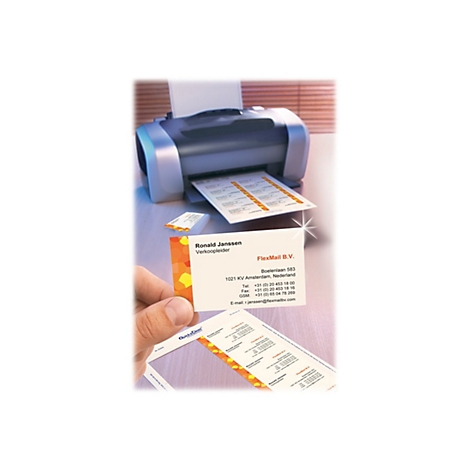 Hand hält bedruckte Visitenkarte neben einem Drucker mit einem Blatt vorgestanzter Etiketten.