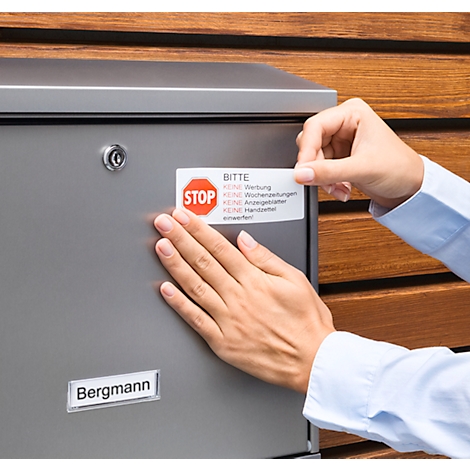 A person is attaching a "No advertising" sticker to a metal mailbox.