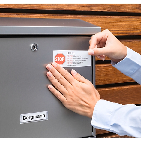 Hands sticking a "No advertising" sign on a metal mailbox. The sign says "STOP" and other instructions.