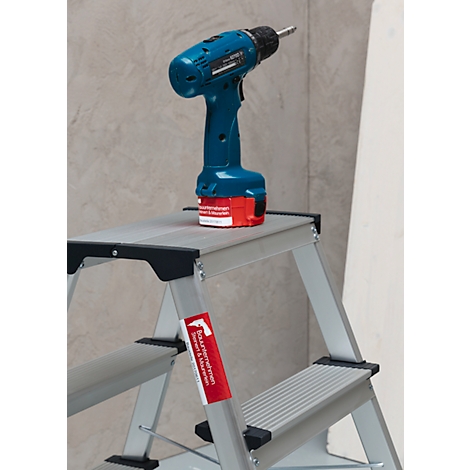 Blue cordless screwdriver on a silver stepladder. A red warning sign on the chair.