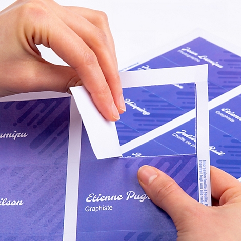 Hände lösen eine Visitenkarte aus einem perforierten Papierbogen mit blauem Design.