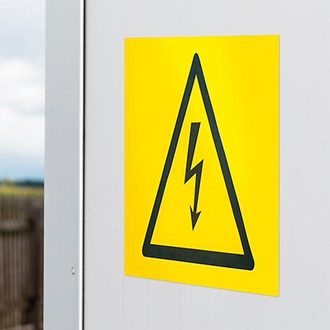 Yellow warning sign with black lightning bolt in a triangle on a white wall.