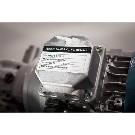 Close-up of a silver engine block with an information sticker. The sticker displays text: Sommer GmbH & Co. KG, München, and technical specifications.
