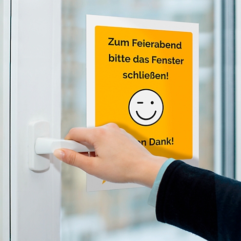 A person operating a window handle next to a sign stating "Close the window at the end of the working day!" with a winking smiley.