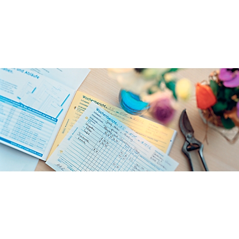Close-up of notes, scissors and flowers on a wooden surface. The notes say 'Wochenbericht'.