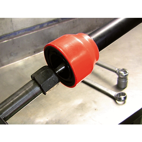 Nahaufnahme einer roten Manschette, die auf einen metallischen Stift aufgesteckt wird. Im Hintergrund liegen Schraubenschlüssel.