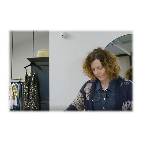 Une femme aux cheveux bouclés regarde des vêtements dans un magasin. Vêtements sur des portants.