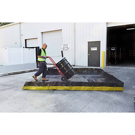 Un homme pousse un tambour avec un chariot dans un bac de rétention noir avec une bordure jaune.