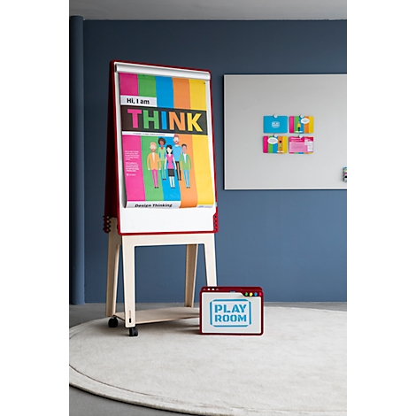 Un tableau de conférence avec une affiche colorée, devant lui une boîte rouge avec "Play Room". Des cartes colorées sont visibles sur le tableau blanc.