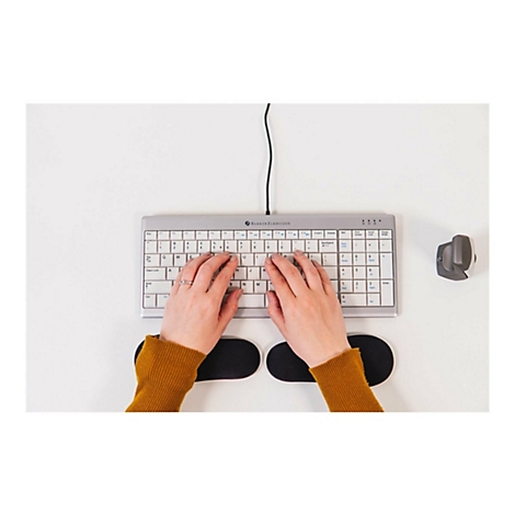 Person tippt auf einer ergonomischen Tastatur. Auf dem weißen Schreibtisch liegen eine Maus und Handgelenkstützen.