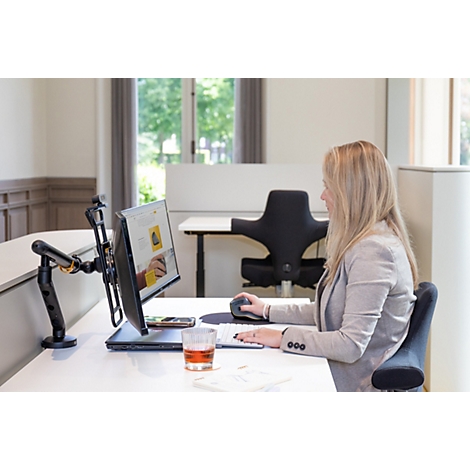Eine Frau arbeitet an einem Schreibtisch. Sie nutzt einen Computer, einen höhenverstellbaren Monitorarm und eine ergonomische Maus.