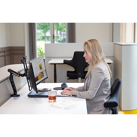 Een vrouw op kantoor werkt aan een computer. Ze typt op een toetsenbord, een glas vloeistof staat op tafel.