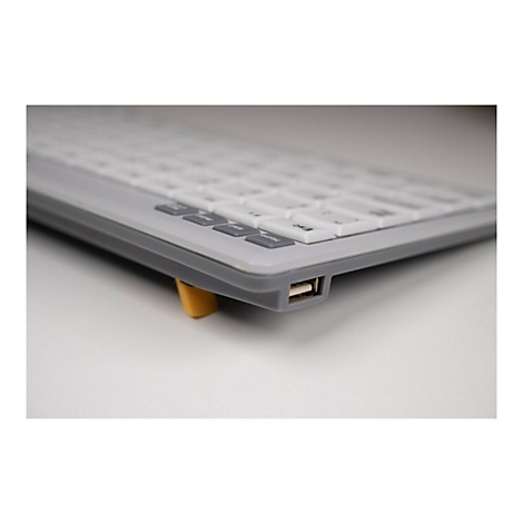 Nahaufnahme der Seite einer grauen Tastatur mit einem gut sichtbaren USB-Anschluss und einem gelben Ständer.