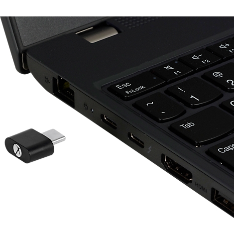 Zwarte USB-C adapter naast een laptop. De adapter is in detail te zien, het toetsenbord staat gedeeltelijk op de foto.