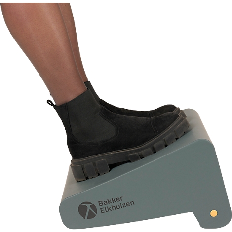 Pieds portant des bottes noires sur un repose-pieds gris. Le repose-pieds porte l'inscription 'Bakker Elkhuizen'.