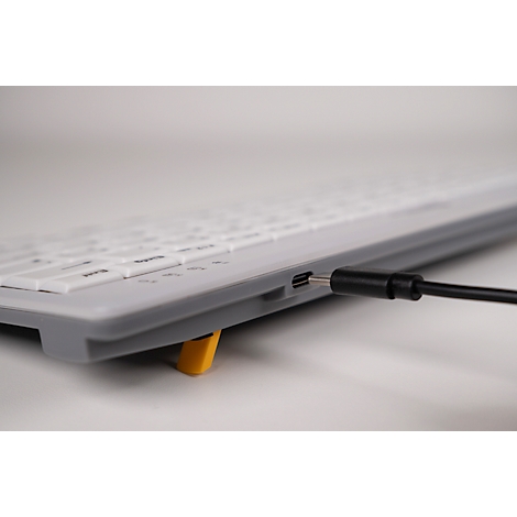 Nahaufnahme einer Tastatur mit angeschlossenem USB-C-Kabel. Gelber Fuß hebt Tastatur an, Detail der Tasten.