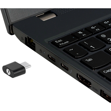 Ein schwarzer USB-C-Adapter neben einem Laptop. Der Adapter und die Laptop-Seite sind im Detail zu sehen, mit Tastatur und Anschlüssen.