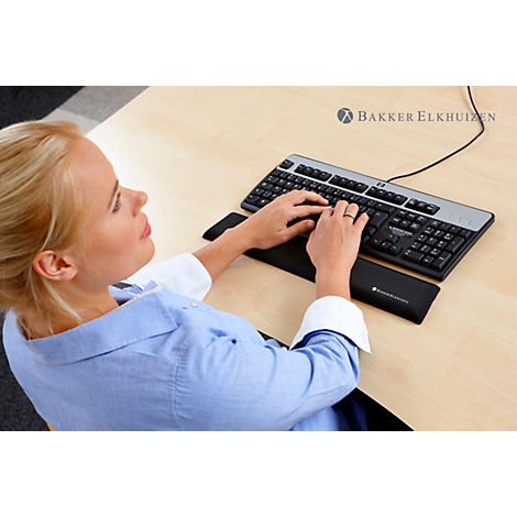 A woman typing on a keyboard. She has blonde hair, is wearing a blue shirt, and is sitting at a light-colored desk.