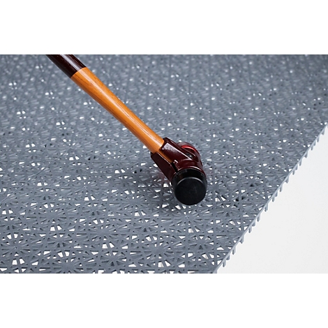 Primer plano del pie de un bastón apoyado sobre una alfombrilla de suelo gris y texturizada.